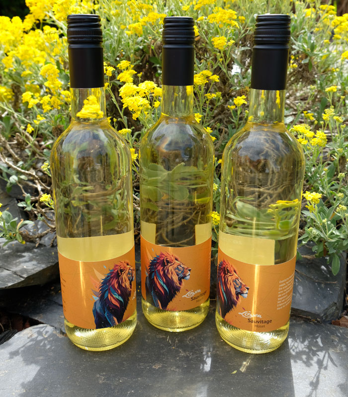 Drei Flaschen Sauvitage nebeneinander auf Schieferstein platziert. Im Hintergrund gelbe Pflanzen.